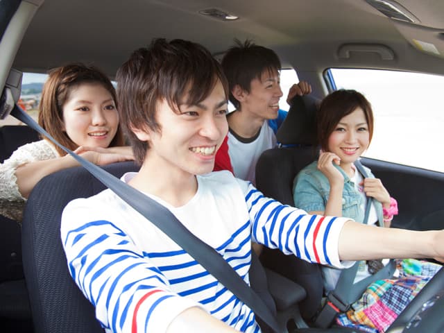 若者4人が笑顔でドライブしている